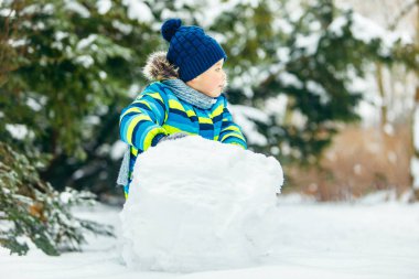 Küçük tatlı çocuk kardan adam yapıyor. yuvarlanan büyük kartopu