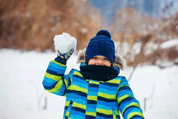 En liten pojke som leker med snö. tillverkning av snöbollar. — Stockfoto