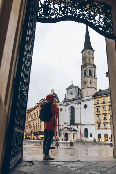 Žena turista ve žluté pláštěnce s batohem při pohledu na kostel svatého Michala — Stock fotografie