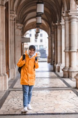 Sarı yağmurluklu şehir turizmiyle sırt çantasıyla gezen kadın turist.