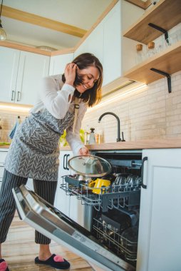 genç güzel kadın bulaşık makinesine tabak koyarak