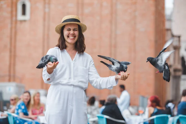 Frau in weißen Kleidern mit Strohhut amüsiert sich mit Tauben auf dem venezianischen Stadtplatz — Stockfoto