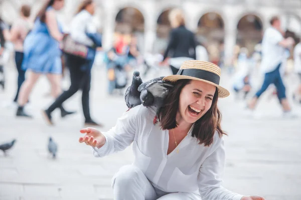 Donna in abiti bianchi con cappello di paglia divertirsi con i piccioni a Venezia piazza della città — Foto Stock