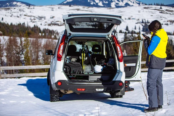 Bagajı kayak ve snowboard malzemeleriyle dolu bir SUV arabasının yanında bir kadın. — Stok fotoğraf