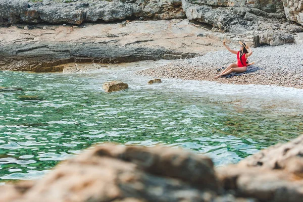 Kırmızı mayo giymiş genç bir kadın Rocky Plajı 'nda oturmuş selfie çekiyordu. — Stok fotoğraf