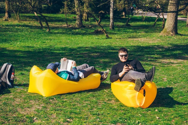 two men friends laying on yellow inflatable mattress reading books surfing internet