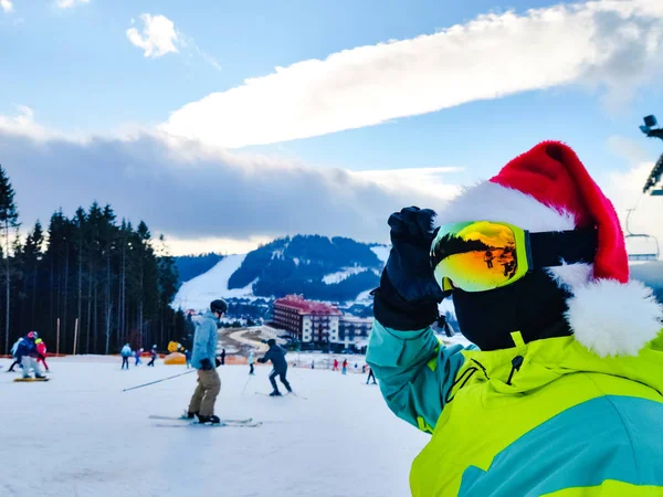 Happy man in ski outfit with santa red christmas hat at winter mountains hill — 스톡 사진