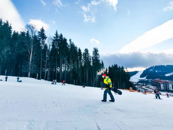 Mann mit Snowboard in roter Weihnachtsmütze geht durch verschneiten Hügel — Stockfoto