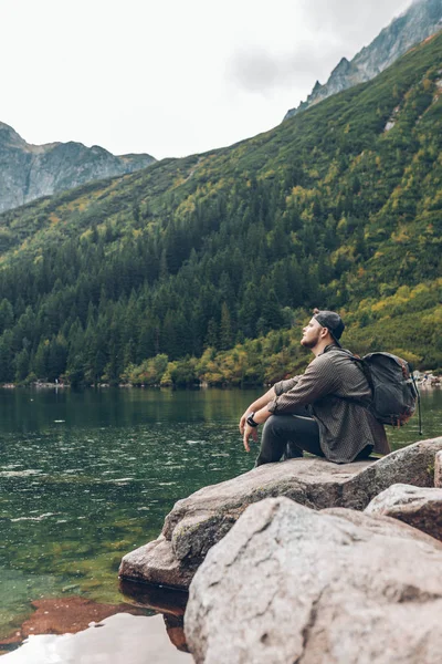 Man sitting on the rock in front of lake in mountains enjoying the view — ストック写真