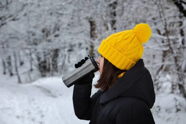 woman in winter outfit drinking warm up drink from refillable mug