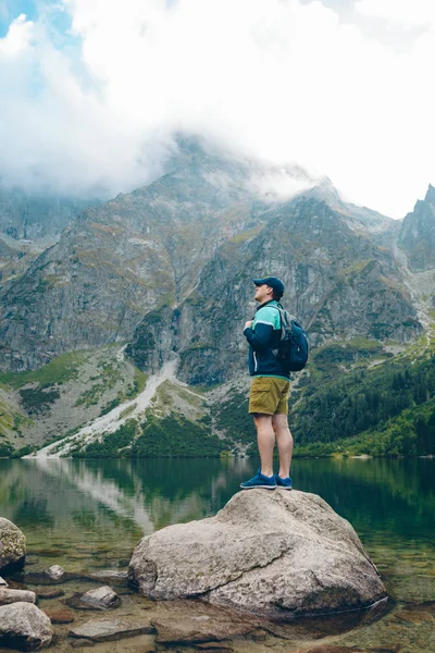 Muž s batohem při pohledu na jezero v horách — Stock fotografie