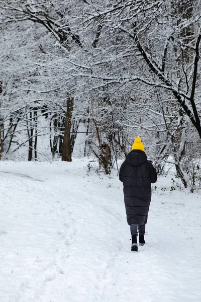 Kvinna i svart vinter rock och gul hatt promenader genom snöade stadsparken — Stockfoto