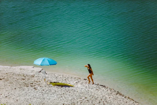 Mulher de maiô andando pela praia de areia guarda-sol azul e cobertor amarelo — Fotografia de Stock