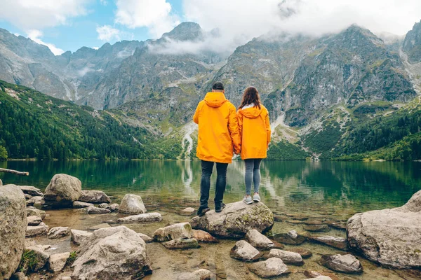 黄色のレインコートを着た男は秋晴れの日にタトラ山脈の湖を見ると — ストック写真