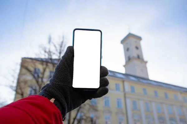 Рука людини в рукавичках, що тримає телефон з білим екраном Львівська ратуша на фоні — стокове фото