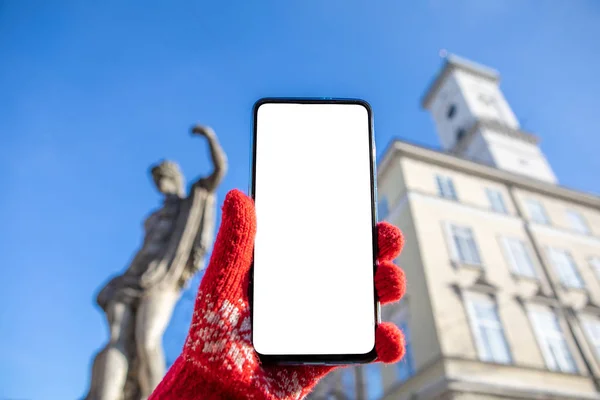 Kobieta ręka w czerwonych rękawiczkach trzymając telefon z białym ekranem lwów ratusz na tle — Zdjęcie stockowe