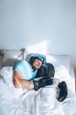 Snowboard kayak yapan bir adam Google ve miğferiyle yatakta.