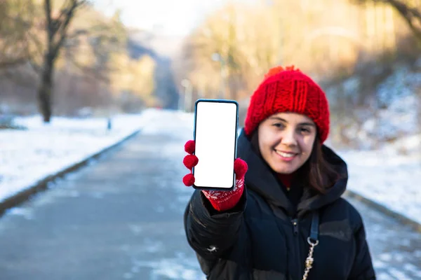 Jovem mulher sorridente em roupa de inverno segurando telefone com tela vazia em branco — Fotografia de Stock