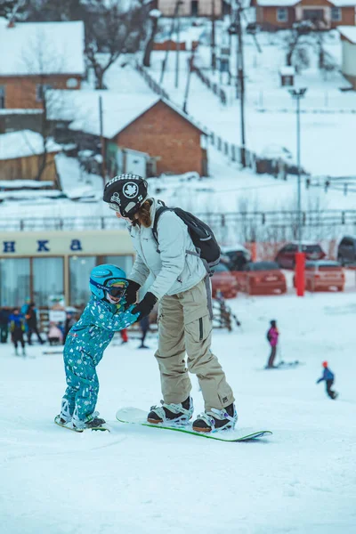 Львов, Украина - 12 января 2019 года: мама учит девочку кататься на сноуборде — стоковое фото