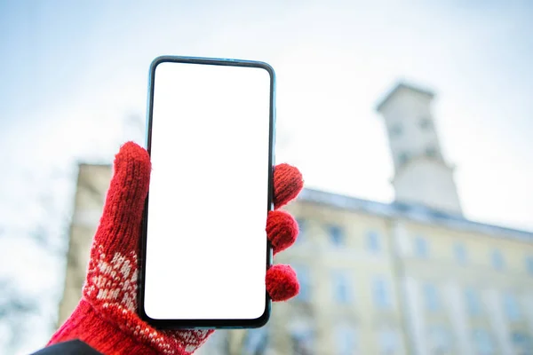 Γυναίκα χέρι σε κόκκινα γάντια κρατώντας τηλέφωνο με λευκή οθόνη lviv δημαρχείο στο παρασκήνιο — Φωτογραφία Αρχείου