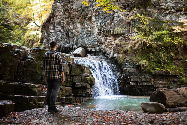 Man in geruit shirt kijkend naar herfst waterval — Stockfoto