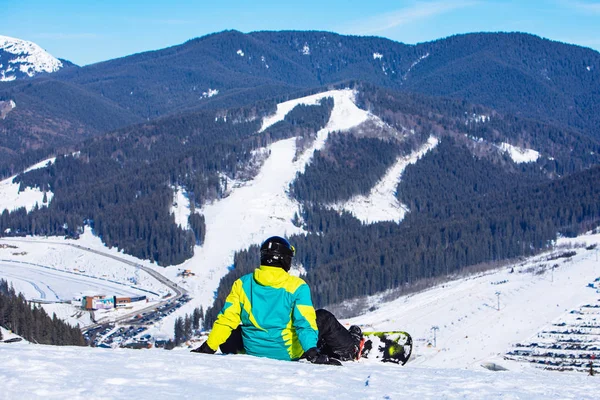 Muž sedí se snowboardem na vrcholu kopce s krásným výhledem — Stock fotografie