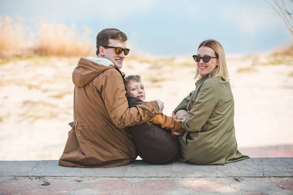 Jovem bela família sentada na praia com vista lago — Fotografia de Stock
