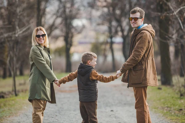 Joven hermosa familia caminando cogido de la mano por el parque de la ciudad —  Fotos de Stock