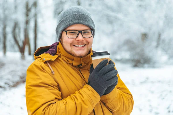 Портрет сильного улыбающегося мужчины, пьющего кофе в снежном городском парке — стоковое фото
