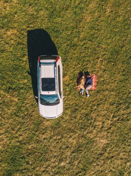 담요 위에 누워 있는 푸른 잔디 밭 부부의 머리 위에 있는 항공 사진 자동차 — 스톡 사진