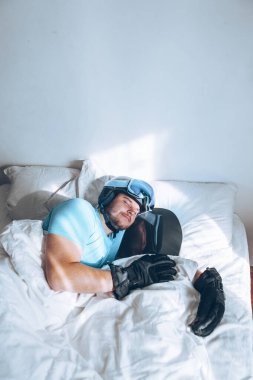 Snowboard kayak yapan bir adam Google ve miğferiyle yatakta.