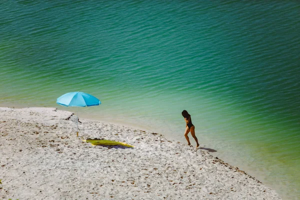 Mujer en traje de baño caminando por la playa de arena sombrilla azul y manta amarilla — Foto de Stock