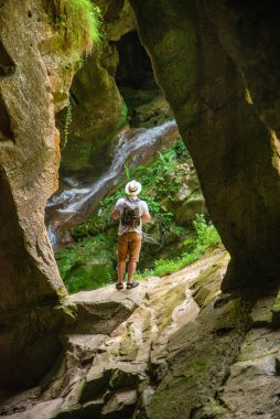 Mağara girişinde sırt çantalı genç ve güçlü bir adam güneş ışığına bakıyor. yaz yürüyüşü konsepti
