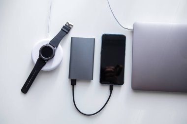 laptop with phone computer mouse and smart watch charging on wireless charger on white table clipart