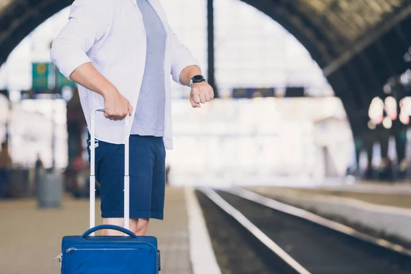 man with bags at railway station looking on watch no face