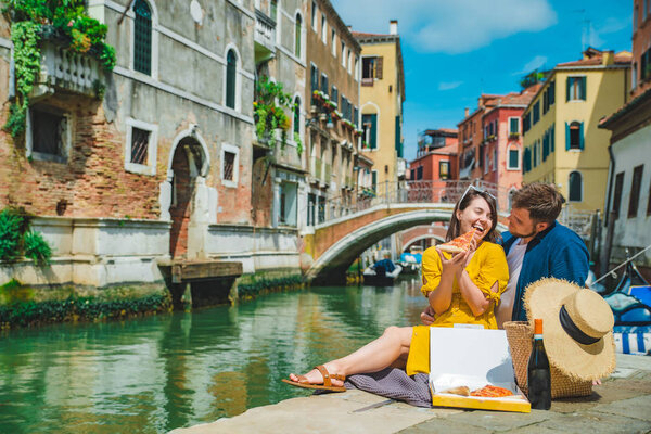 couple having date at pier with beautiful view of venice canal eating pizza