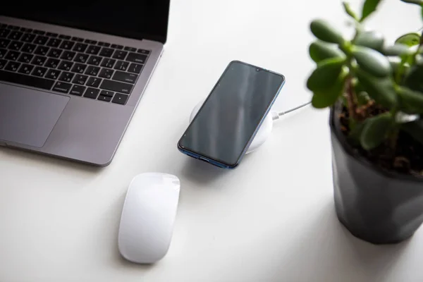 overhead view of computer mouse with laptop and cellphone on wireless charger black and white flatlay