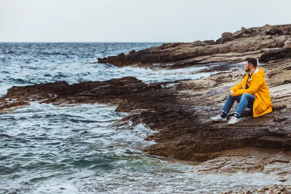Homem Sentado Capa Chuva Amarela Praia Rochosa Olhando Para Tempo — Fotografia de Stock