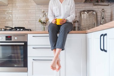 Mutfak masasında oturan kadın telefon ve sarı bardakla. Çay içiyorum.