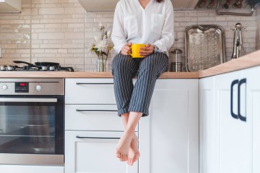 Mutfak masasında oturan kadın telefon ve sarı bardakla. Çay içiyorum.