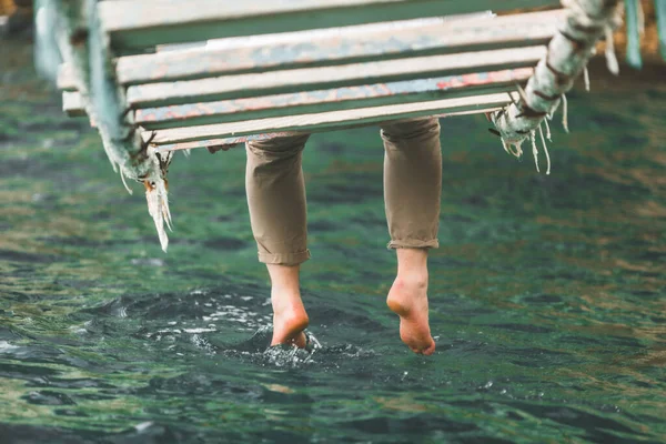Фотография Урожая Человек Сидит Подвесном Мосту Положить Ноги Морской Воде — стоковое фото