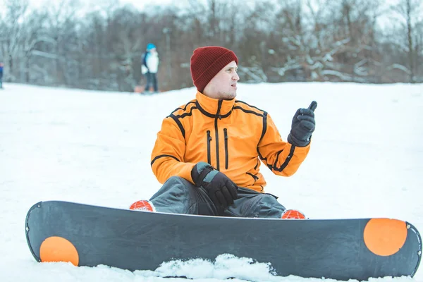 拿着雪板的年轻人坐在雪地上休息 冬季活动生活方式 — 图库照片