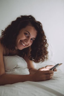 Yatakta kıvırcık saçlı, ev hayatı olan genç ve güzel bir kadın.