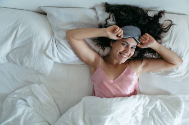 Sabahın köründe uyanan bir kadın. uyku maskesi beyaz çarşaflar