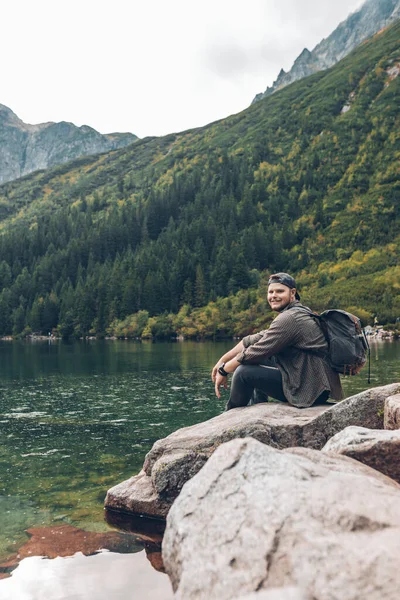 山の中の湖の前の岩の上に座ってハイキングのコンセプトを楽しんでいる男 — ストック写真