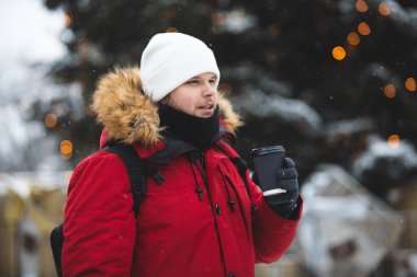 Adam dışarıda kağıt bardaktan kahve içiyor. Kış zamanı kırmızı ceketi ısıtıyor.