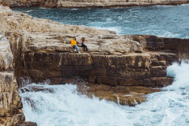 uçurumda fırtına denizine bakan iki genç yetişkin kadın. bulutlu hava