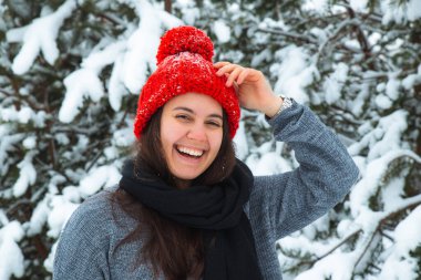 Arka planda bubo köknar ağacı olan kırmızı şapkalı, kışın gülümseyen genç kadın portresi. şık konsept