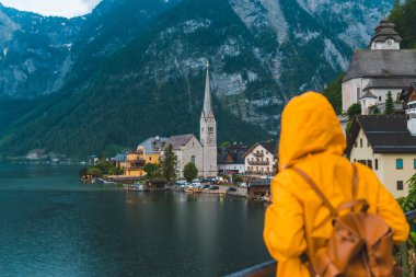 Sarı yağmurluklu kadın Hallstatt City panoramik manzarasına bakıyor