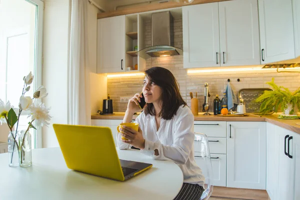 Mulher Sentada Cozinha Trabalhando Laptop Falando Sobre Telefone Beber Chá — Fotografia de Stock